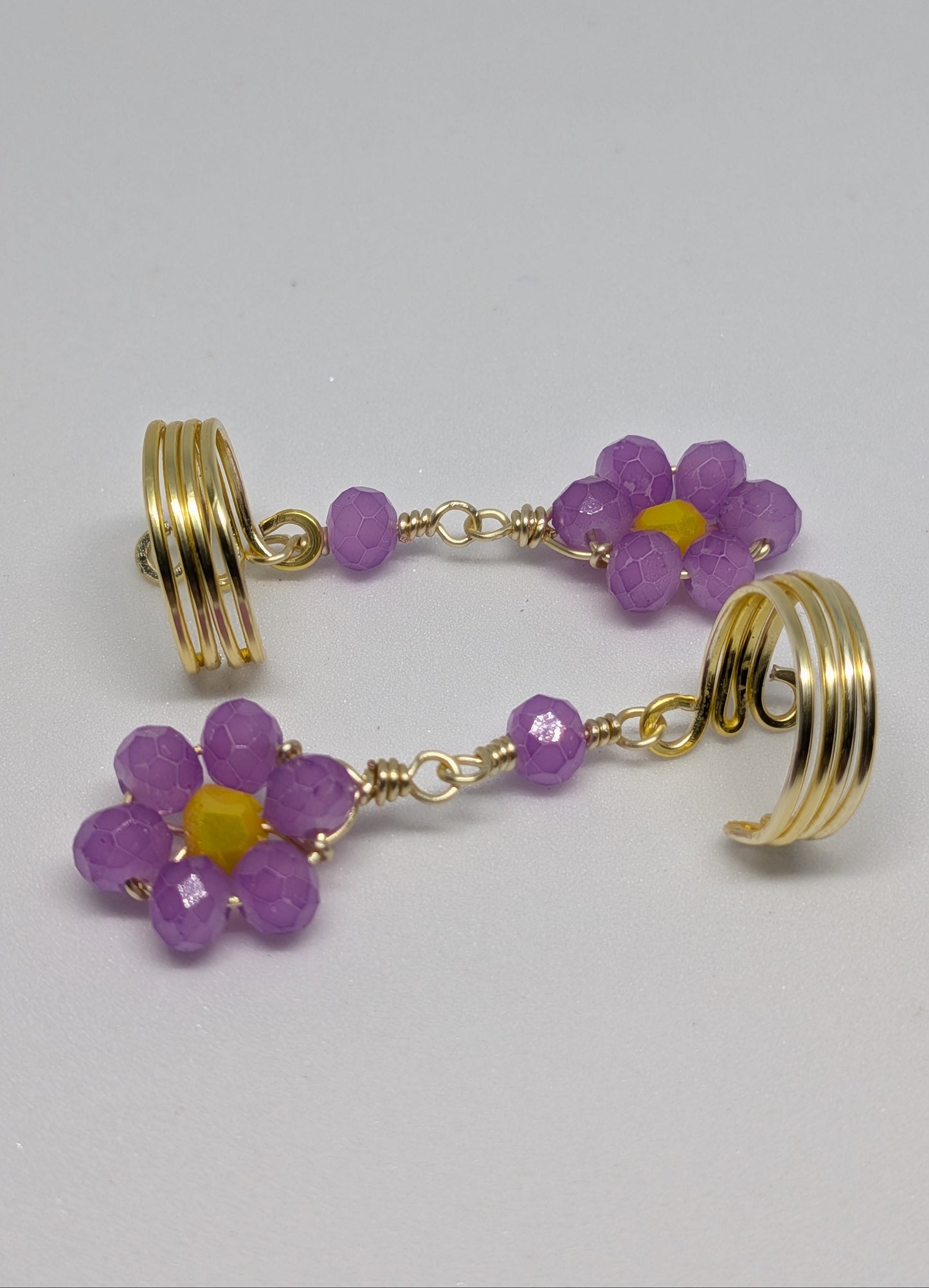 Ein Paar Earcuffs in Hellgold mit Blumenanhänger in sommerlich leuchtendem Flieder
