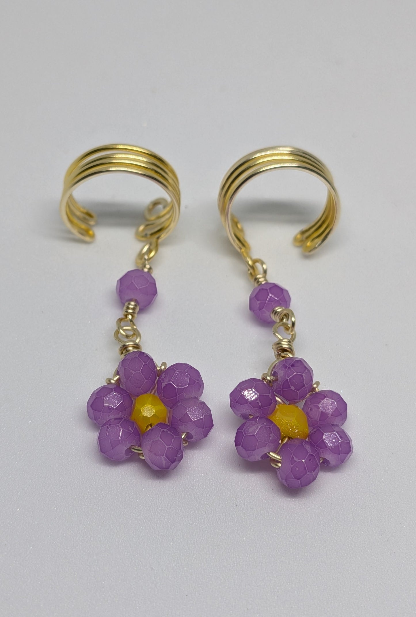 Ein Paar Earcuffs in Hellgold mit Blumenanhänger in sommerlich leuchtendem Flieder